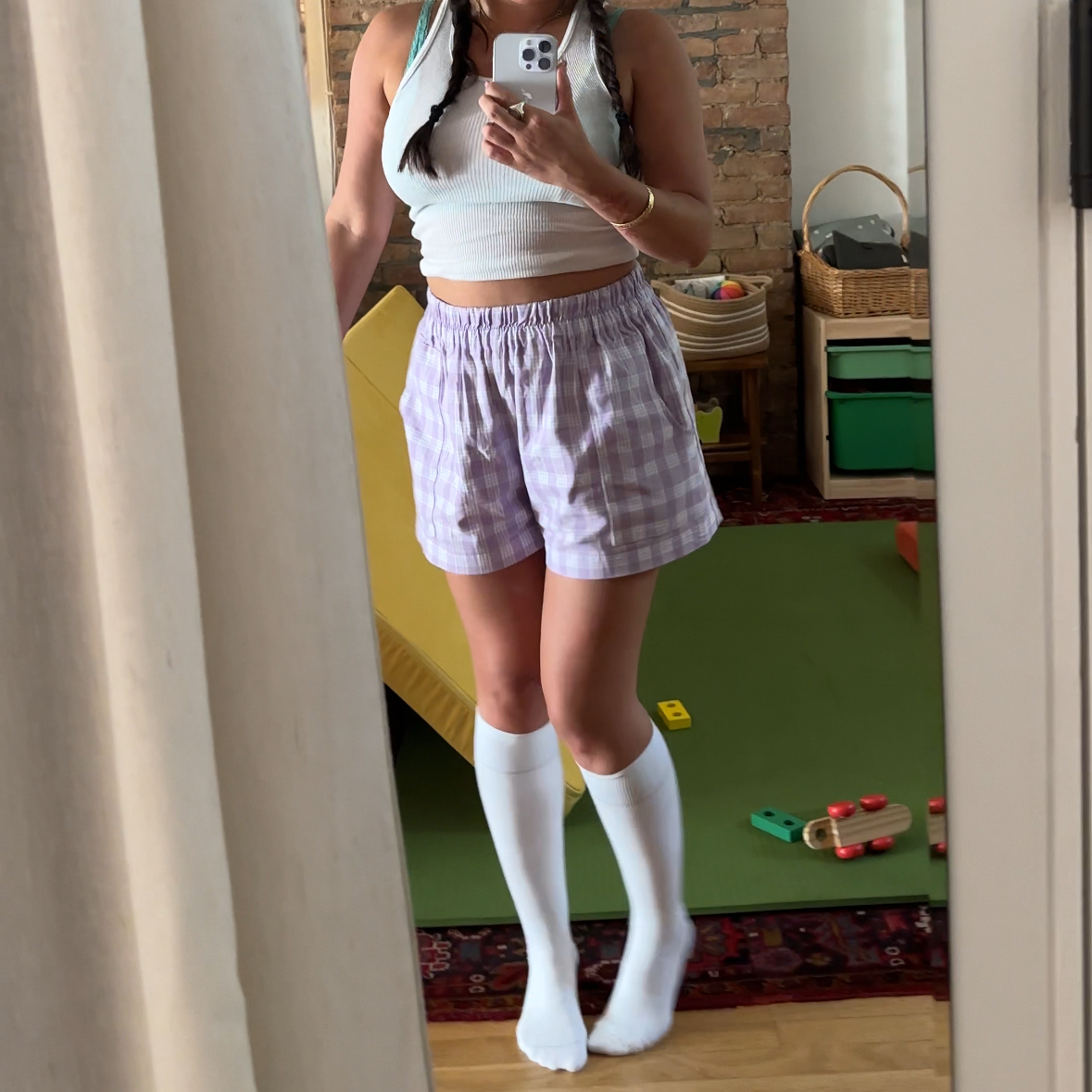 Person taking a mirror selfie wearing a white crop top, plaid shorts, and knee-high socks.