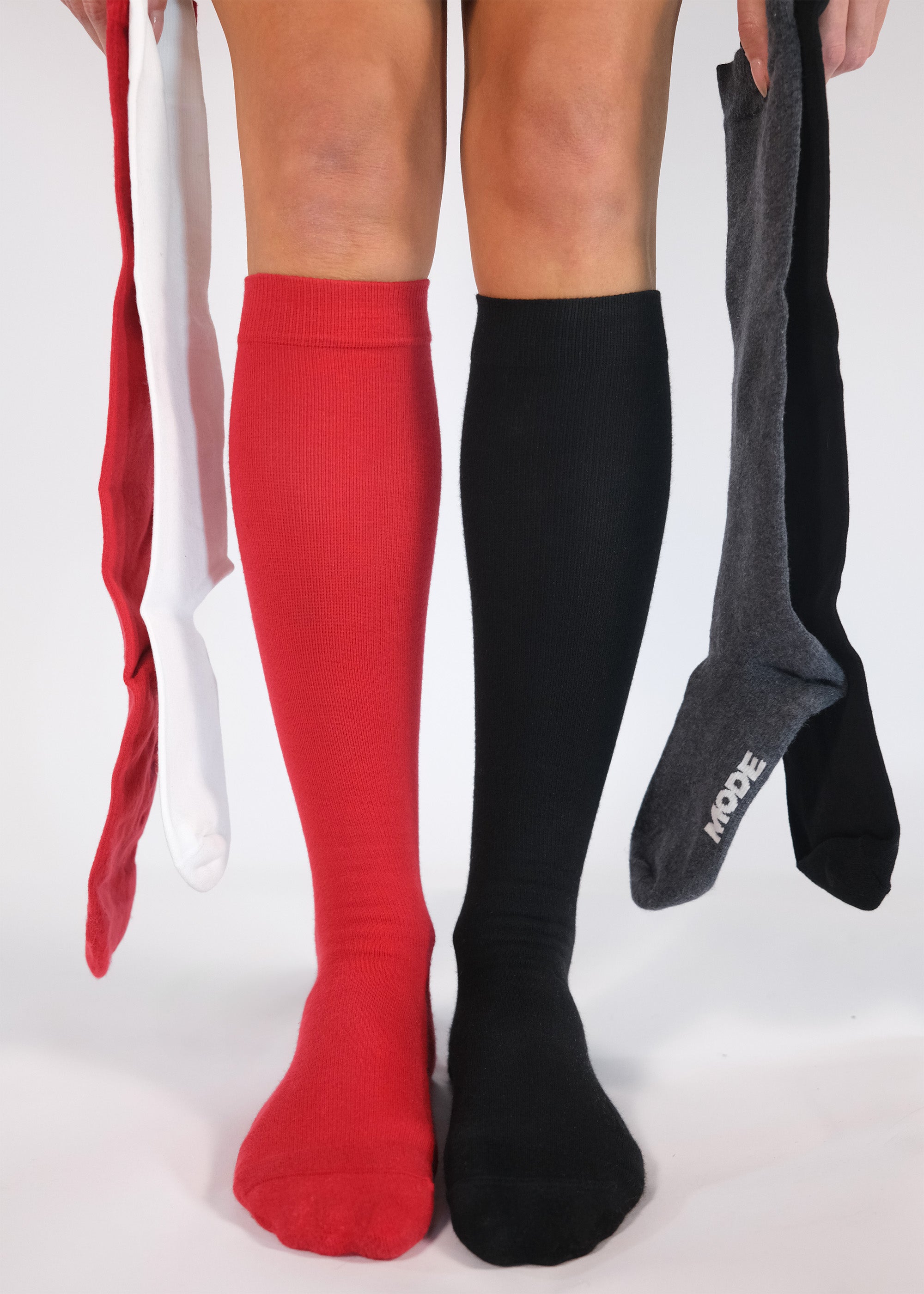 Red, black, and gray knee-high socks held by a person on a white background