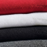 A close-up stack of folded knit garments in multiple colors, including red, white, black, and gray, showing the ribbed fabric texture.
