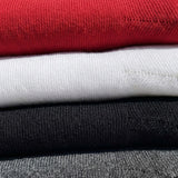 A close-up stack of folded knit garments in multiple colors, including red, white, black, and gray, showing the ribbed fabric texture.