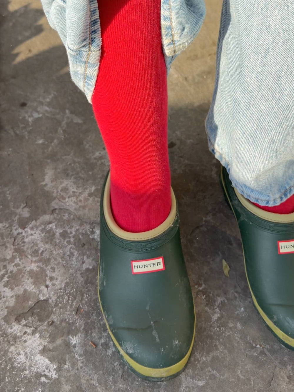 Green Hunter boots with red knee high compression socks on a concrete floor