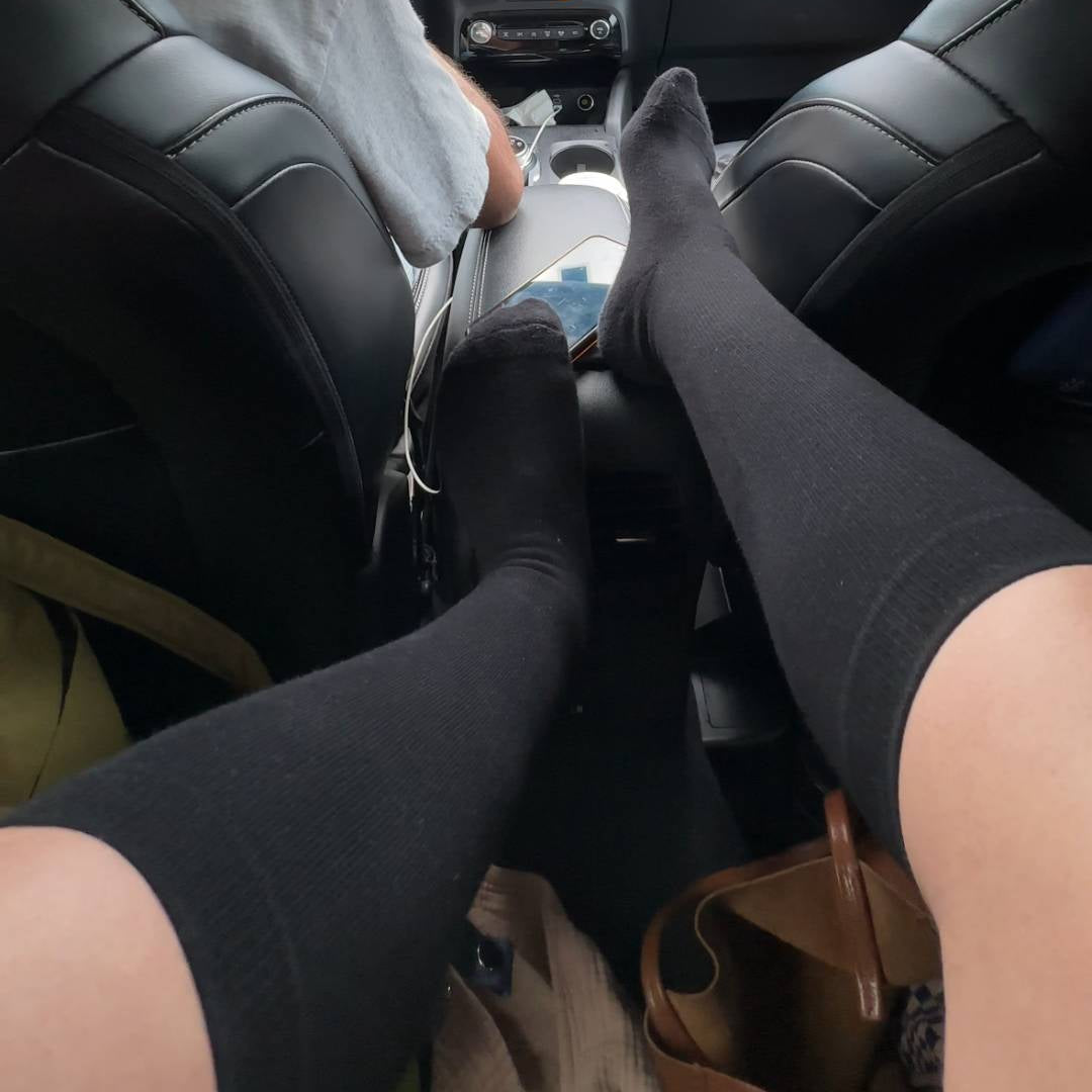 Person sitting in a car wearing black knee high compression socks with a GPS device on the dashboard