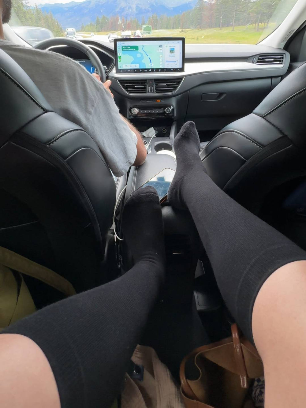Person sitting in a car wearing black knee high compression socks with a GPS device on the dashboard