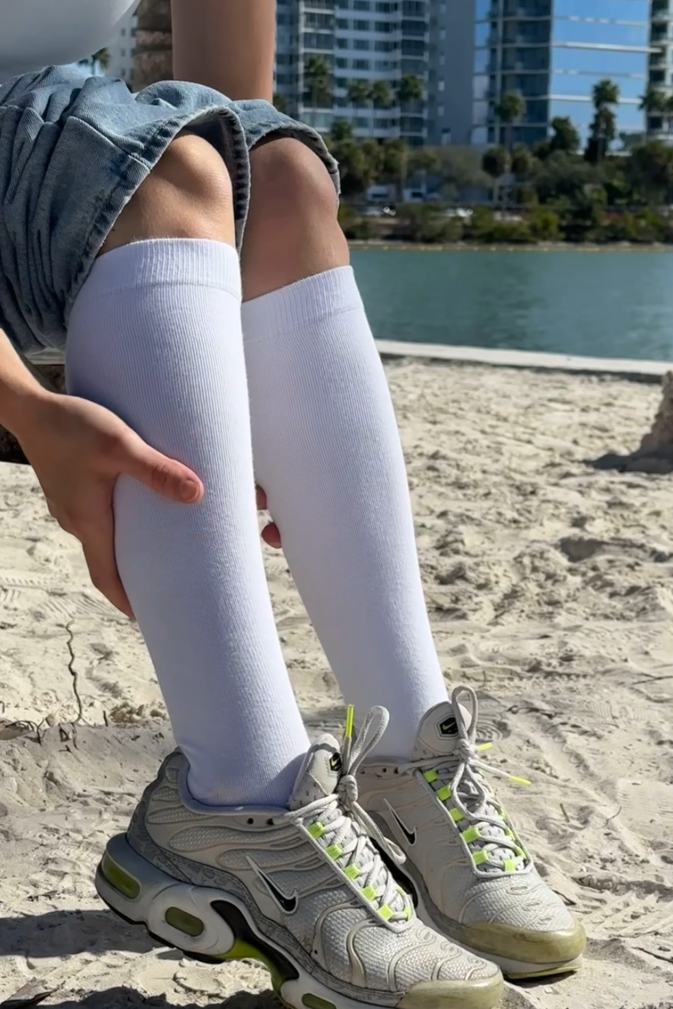 woman wearing white cotton knee high compression socks with denim jeans on top and white nike sneakers taken on the sand in florida