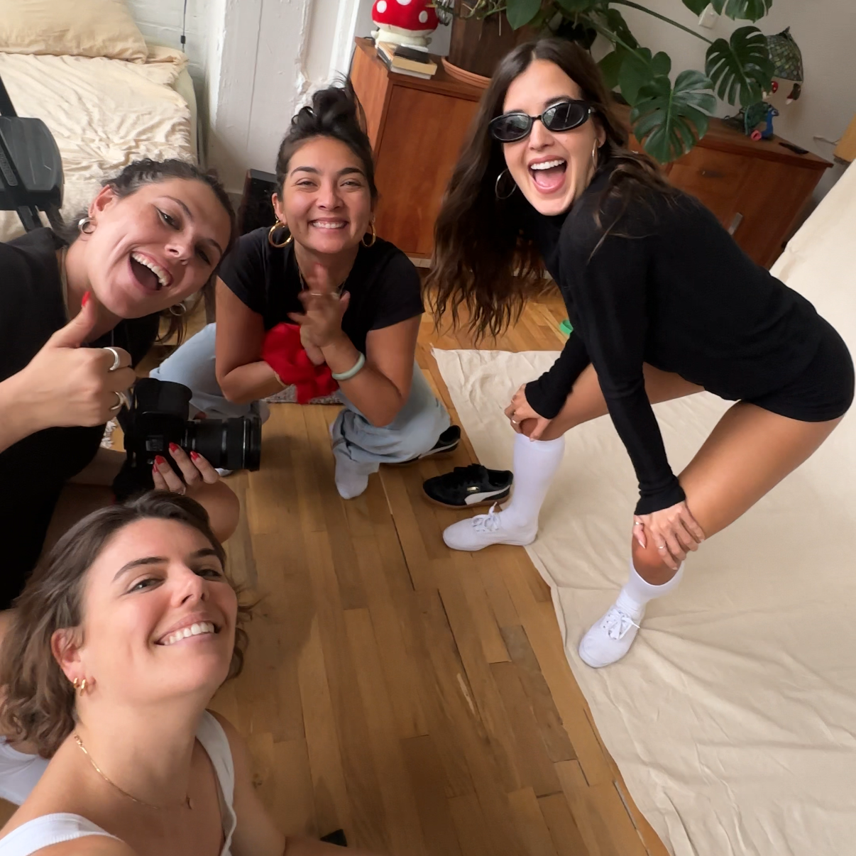 Four friends posing for a selfie in a living room with plants and furniture.