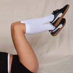 Person wearing black sneakers with tan soles and white knee-high compression socks on a beige background