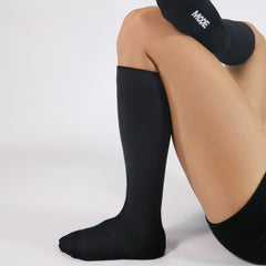 Person wearing black knee-high compression socks on a white background