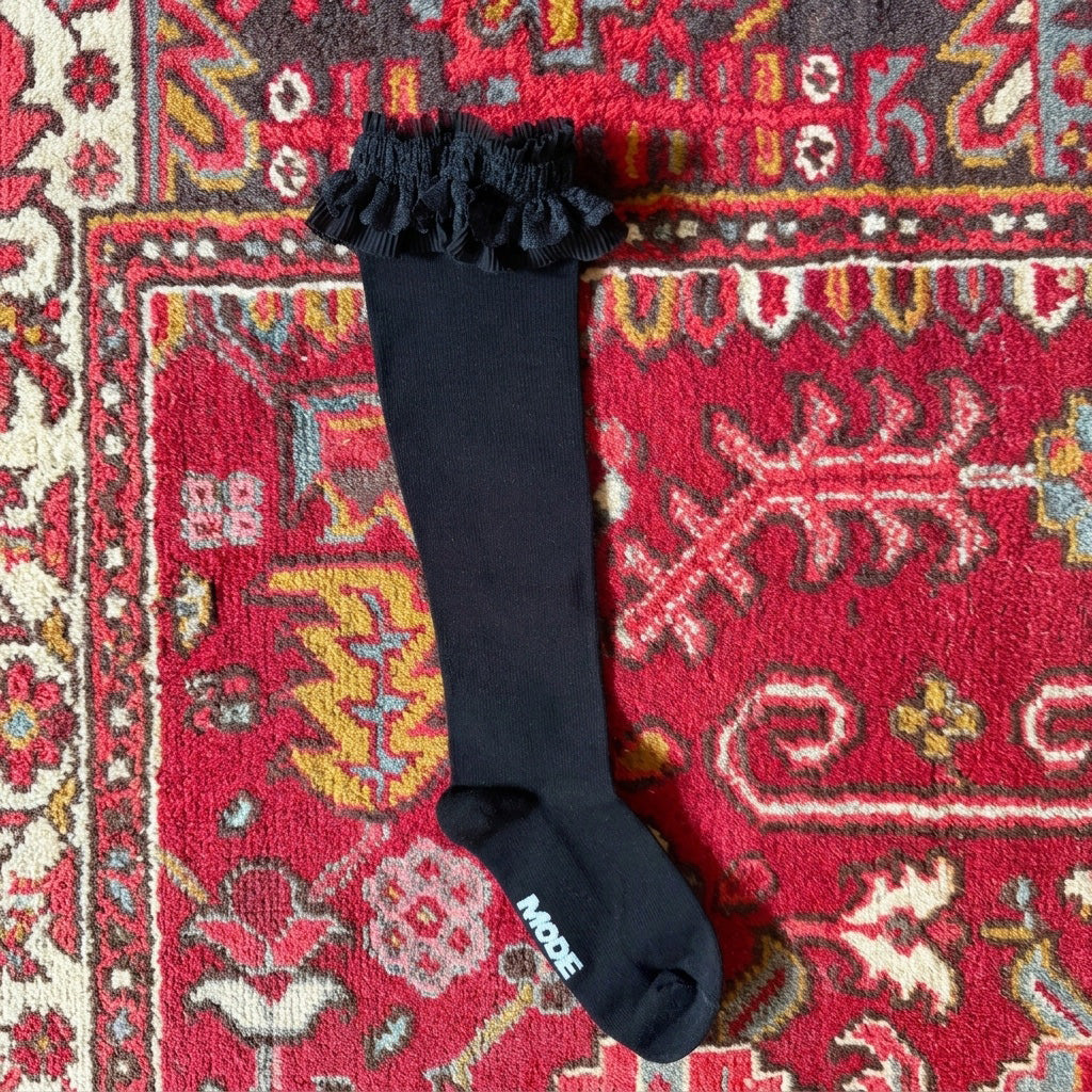 Black knee-high socks with ruffles on a colorful patterned rug