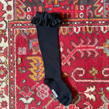 Black knee-high socks with ruffles on a colorful patterned rug