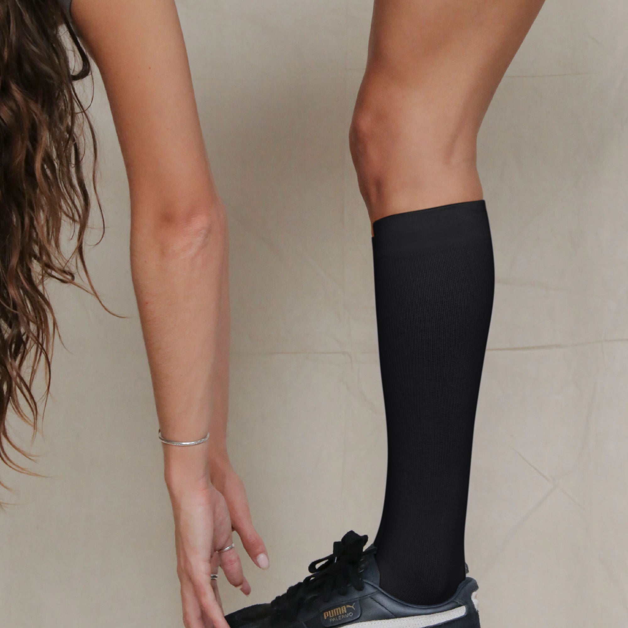 Person wearing black knee-high socks and a dark sneaker on a neutral background