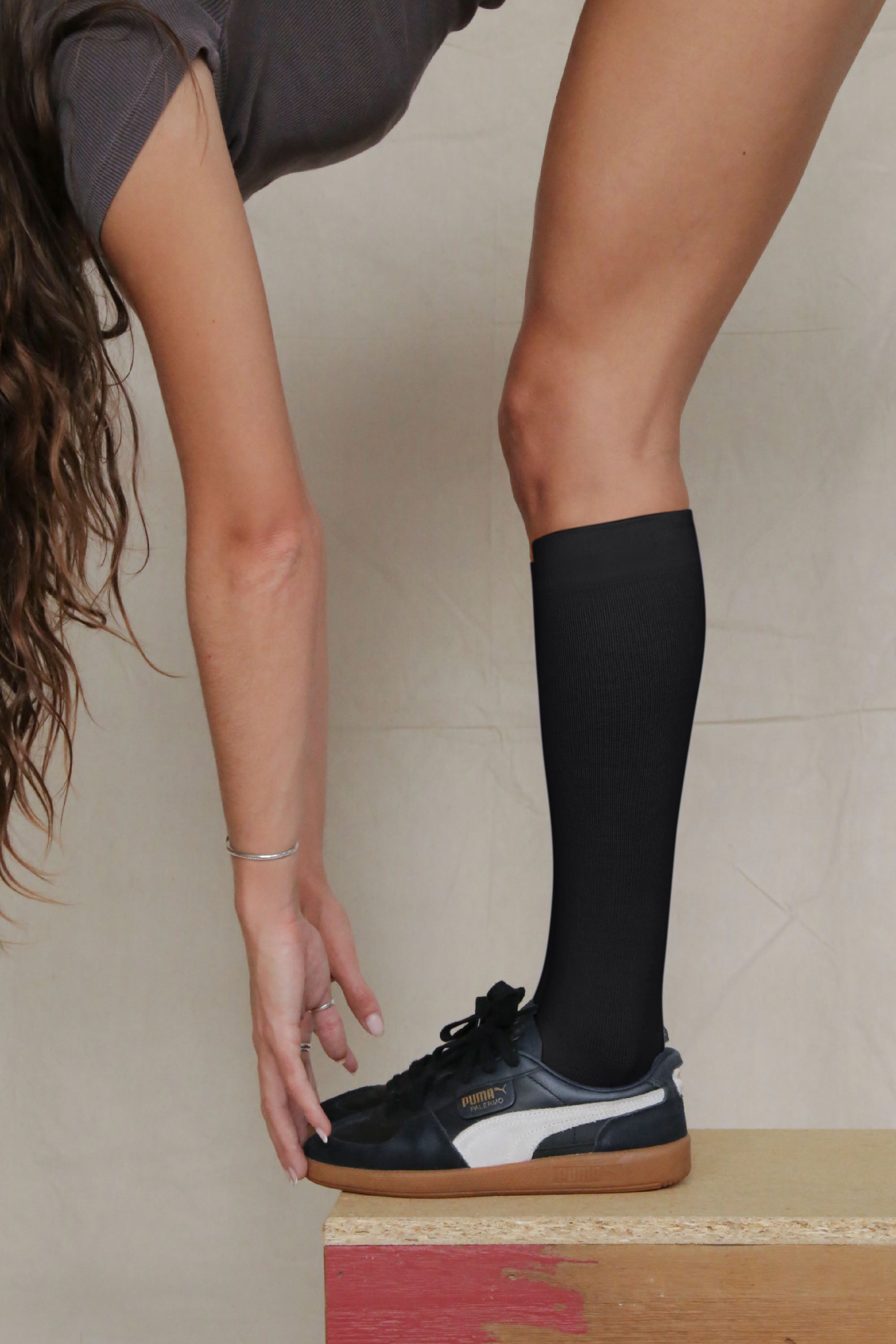 Person wearing black knee-high socks and a dark sneaker on a neutral background