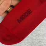 Red sock with 'MODE' branding held by a hand on a gray background