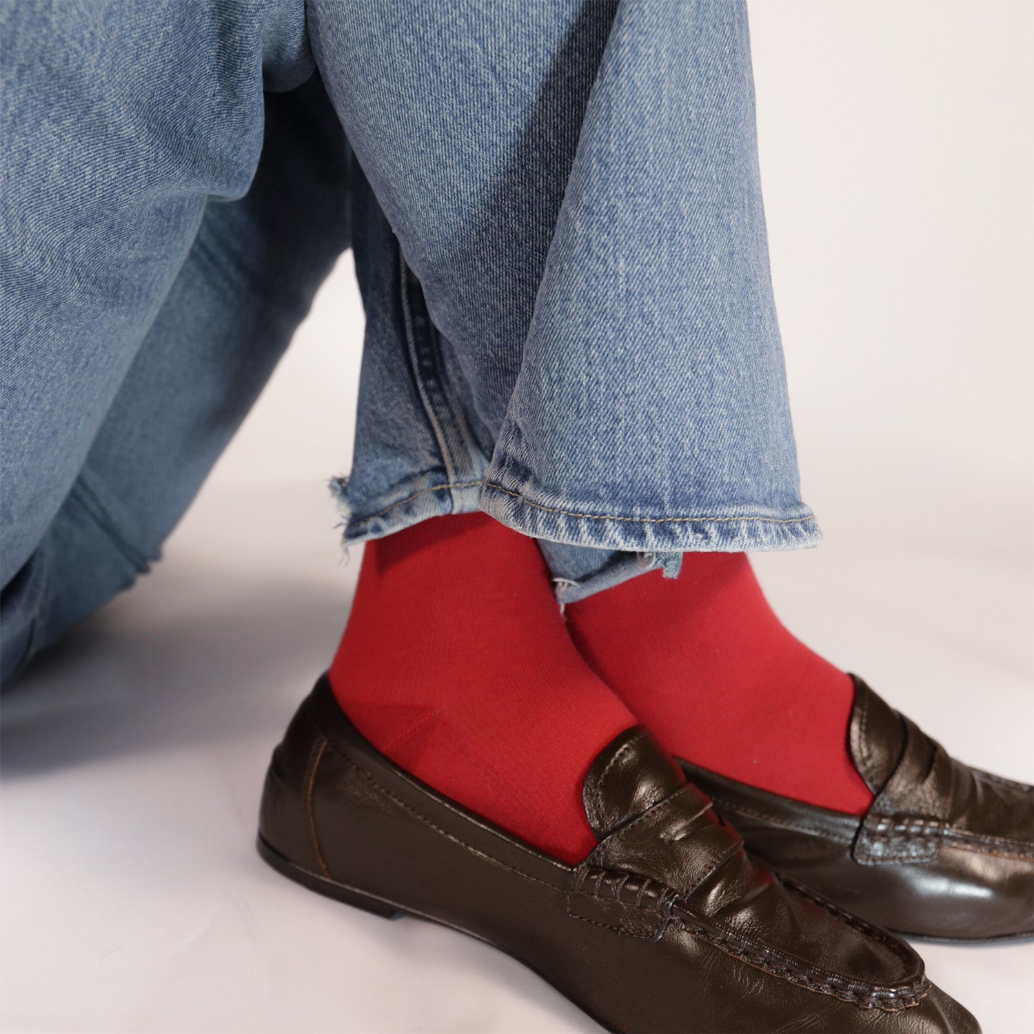 Red compression socks with blue jeans and brown shoes on a neutral background.