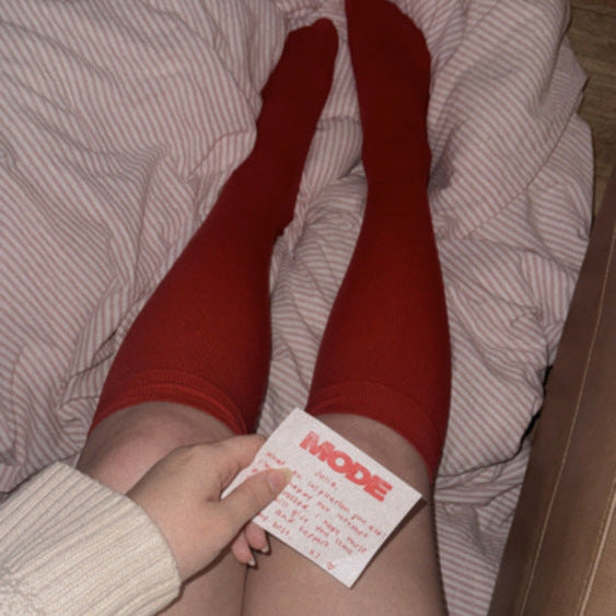 Person wearing red compression socks with a MODE compression sock in the mail, sitting on a couch.